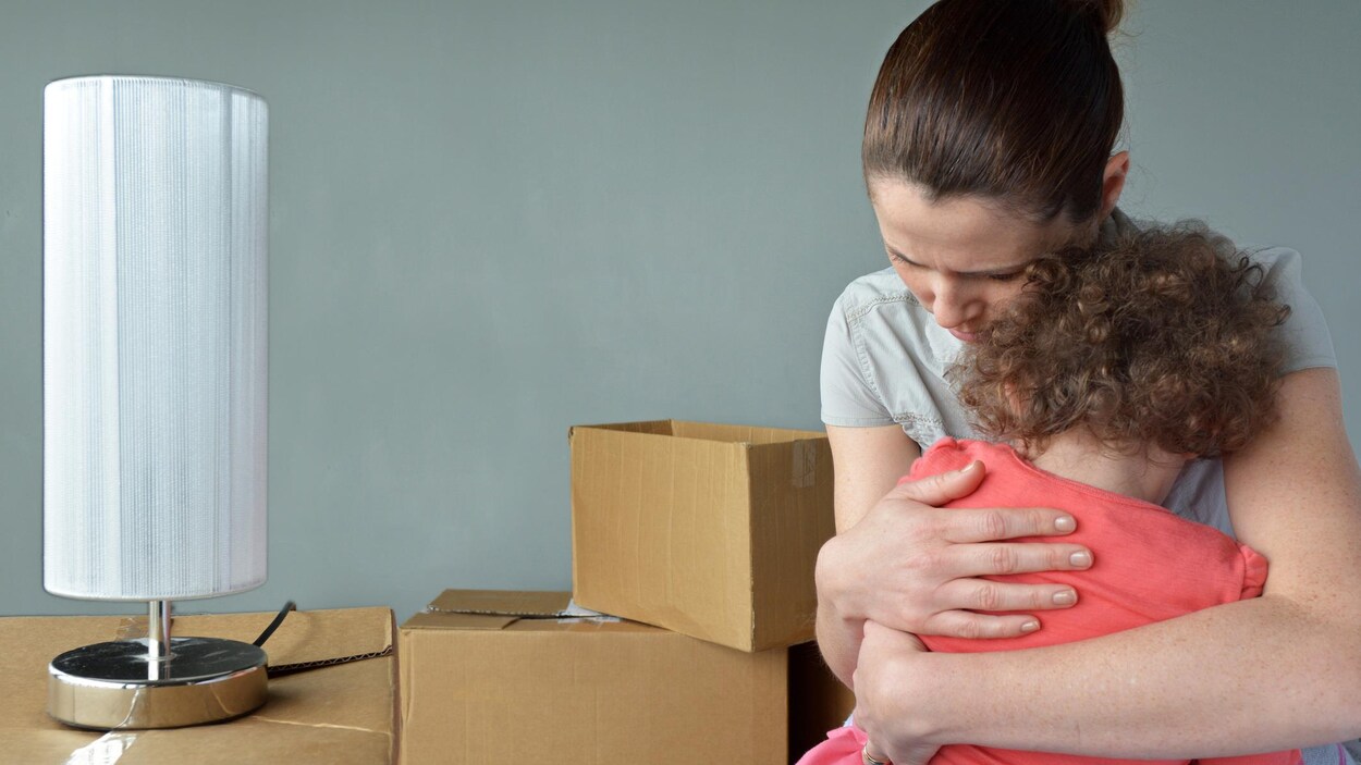 Une femme tient un enfant dans ses bras alors qu'elle a des boîtes de carton autour d'elle
