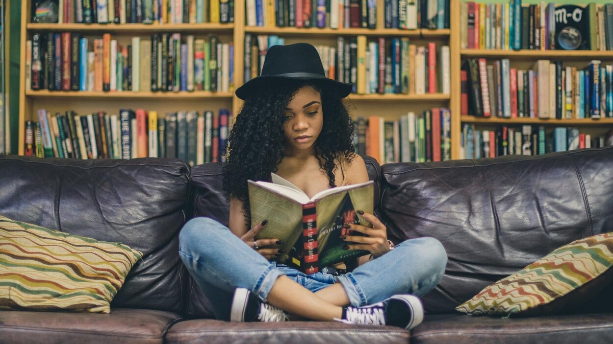 Une jeune femme lit, assise en tailleur sur un sofa.