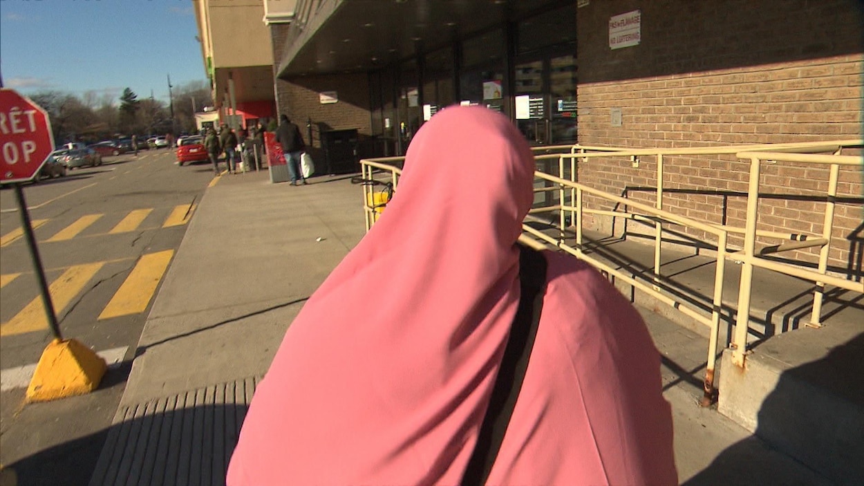 Une femme portant un niqab rose marche sur la rue.