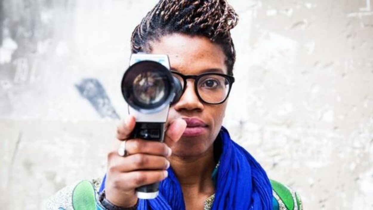 Une femme noire tend devant elle l’objectif d’une caméra.