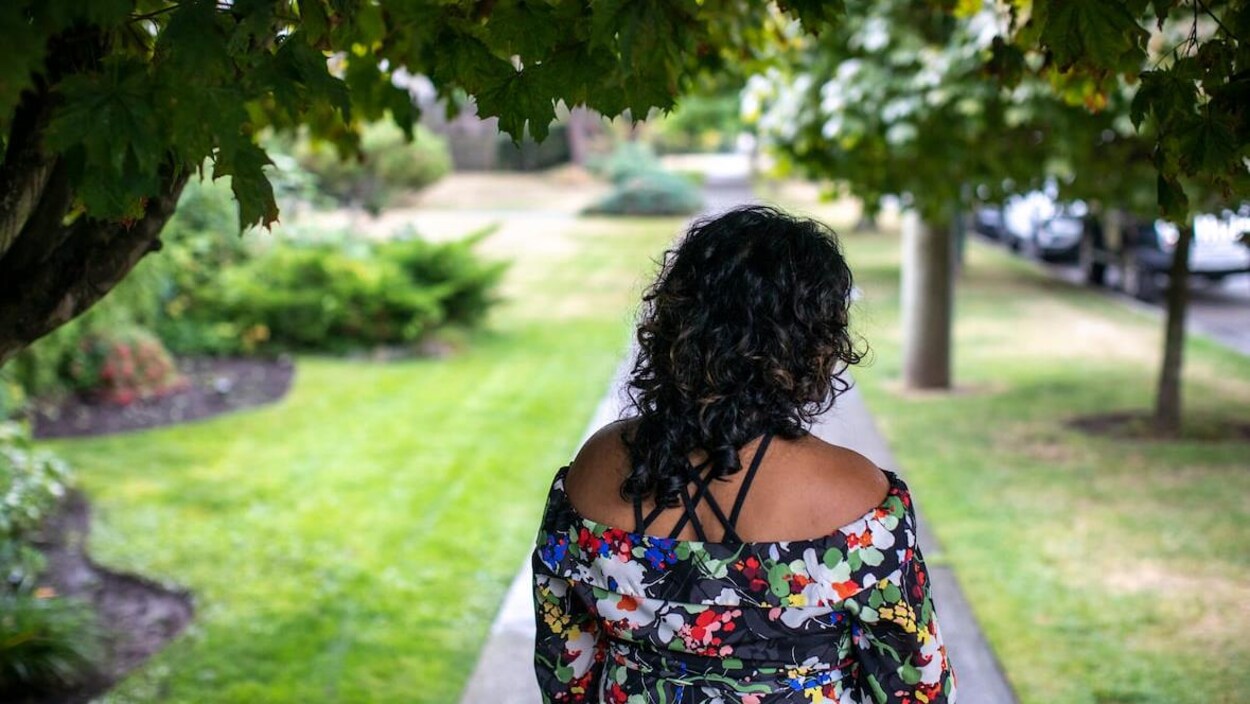 Une femme portant une robe fleurie marche dans un parc à Vancouver, le dos tourné à la caméra.