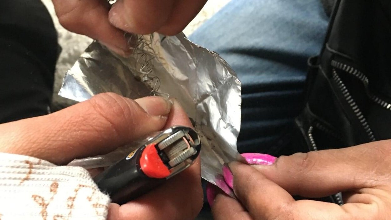 Gros plan sur des mains qui tiennent un morceau de papier aluminium, un briquet et un ressort métallique.