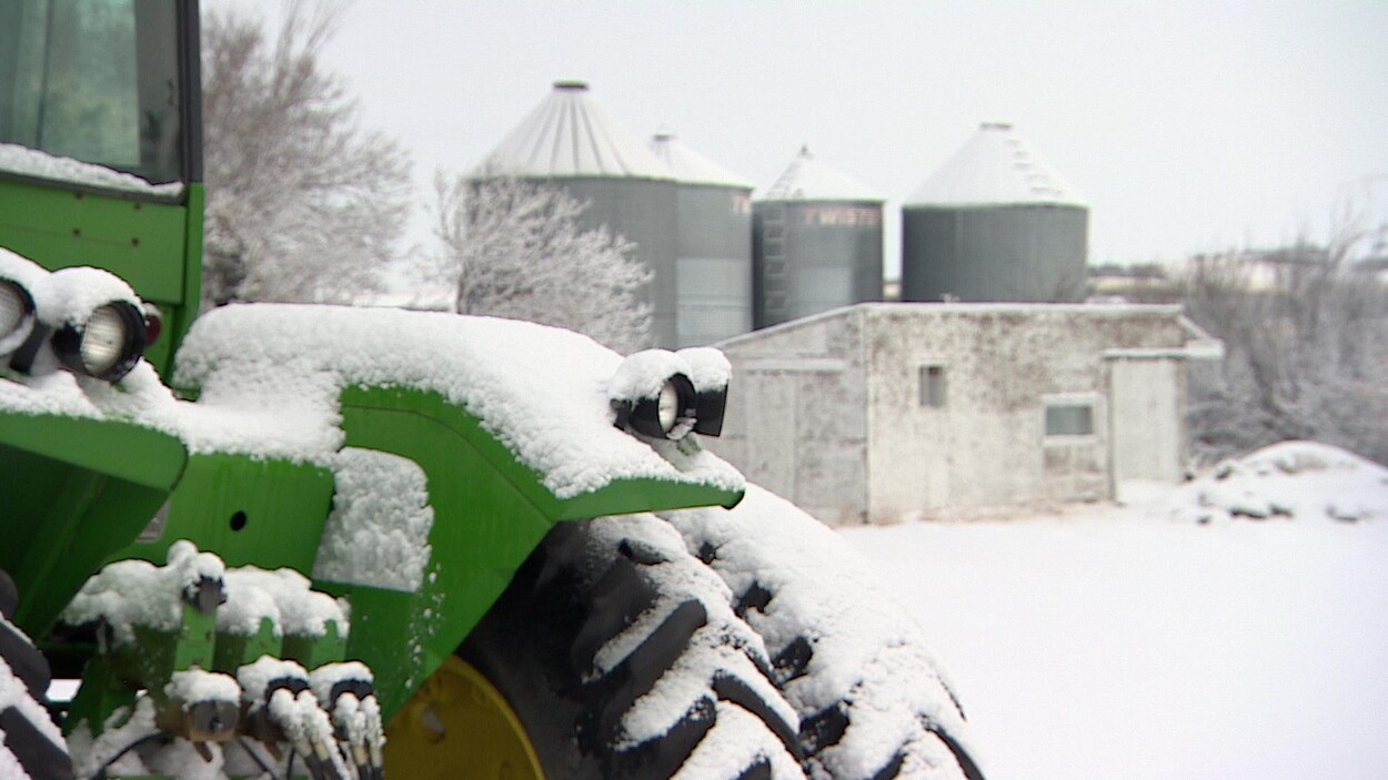 Un tracteur vert enneigé devant un cabanon et des installations agricoles, en temps de neige. Un tracteur vert enneigé devant un cabanon et des installations agricoles, en temps de neige.