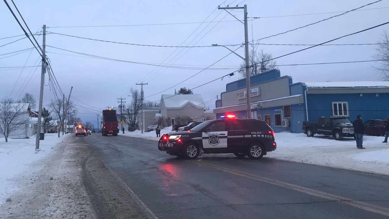 Un véhicule de police barre la route, où un camion avec la benne levée est en contact avec des fils électriques.