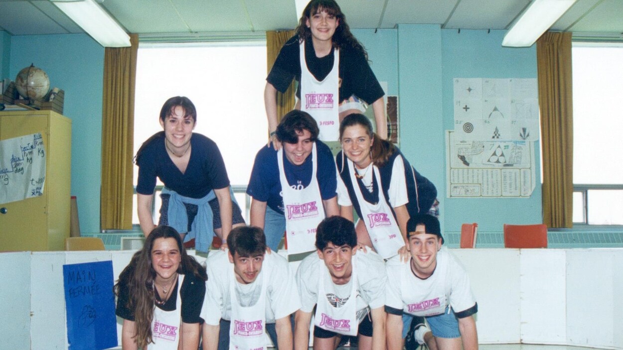 8 jeunes font une pyramide humaine dans une salle de classe : 4 en bas, 3 au milieu et une jeune fille en haut. 8 jeunes font une pyramide humaine dans une salle de classe : 4 en bas, 3 au milieu et une jeune fille en haut.