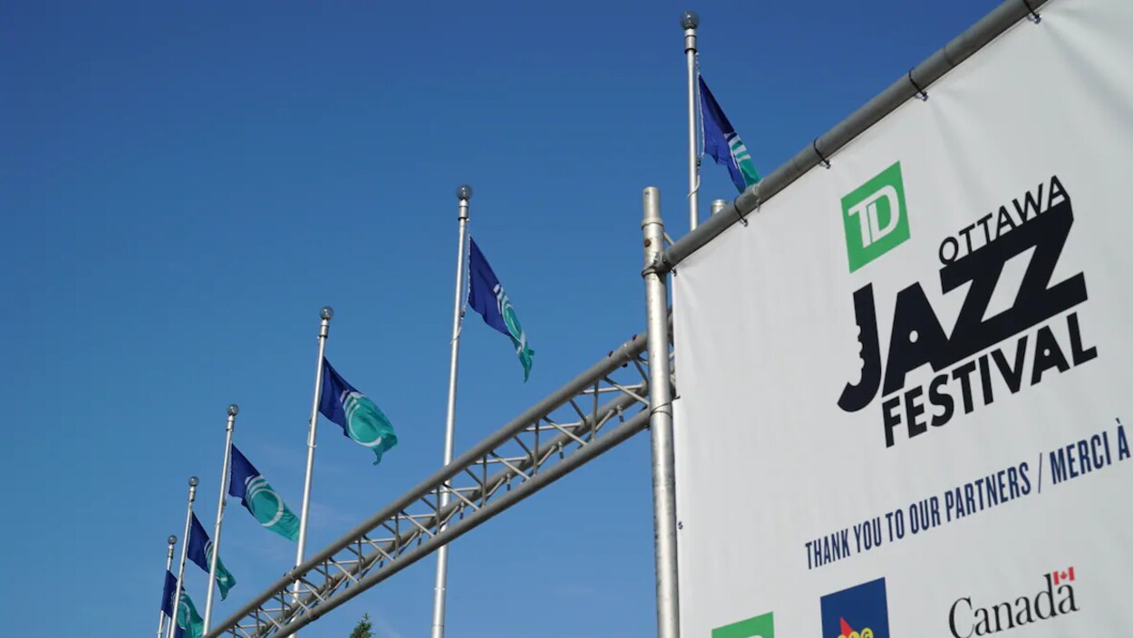 Une enseigne du Festival de jazz d'Ottawa avec, en arrière-plan, des drapeaux de la Ville d'Ottawa.