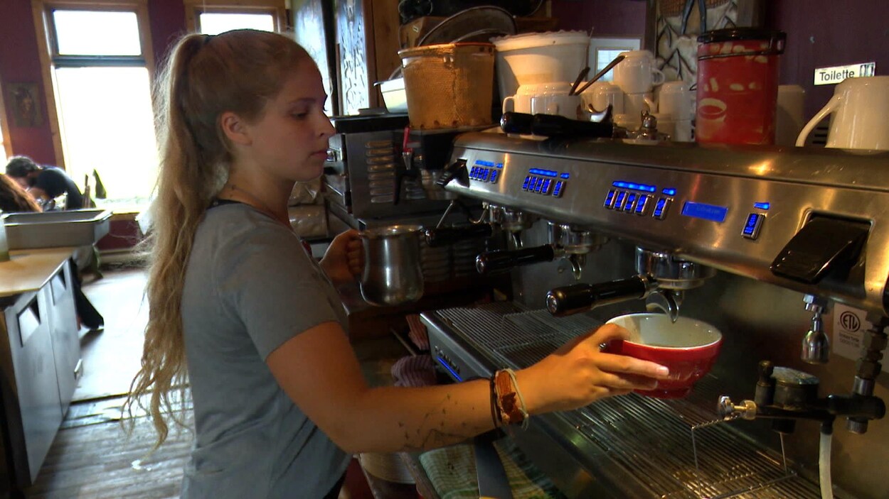La jeune dame aux cheveux blonds tient un bol devant la machine à café.