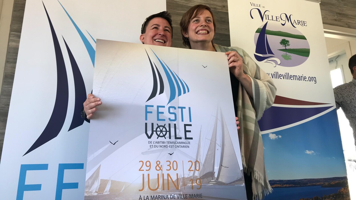 Deux femmes sourient en tenant une affiche du Festivoile de l'Abitibi-Témiscamingue et du Nord-Est ontarien.