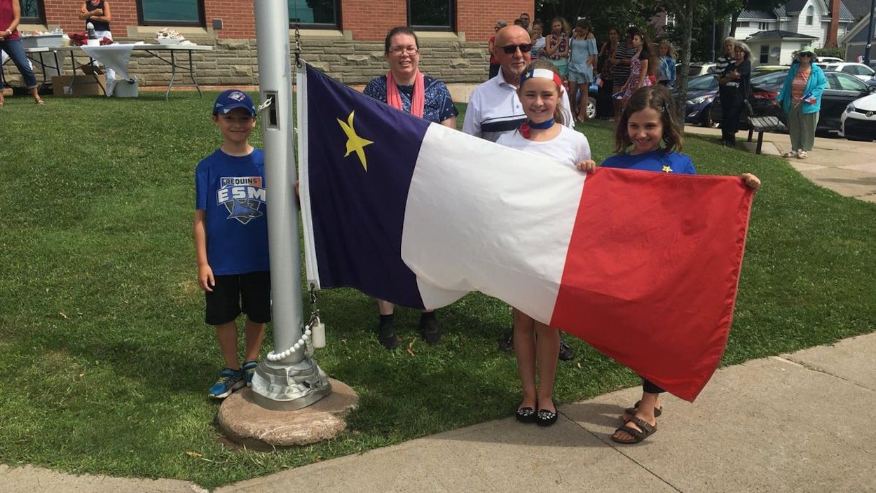 Groupe de personnes devant un drapeau acadien que l'on va hisser.