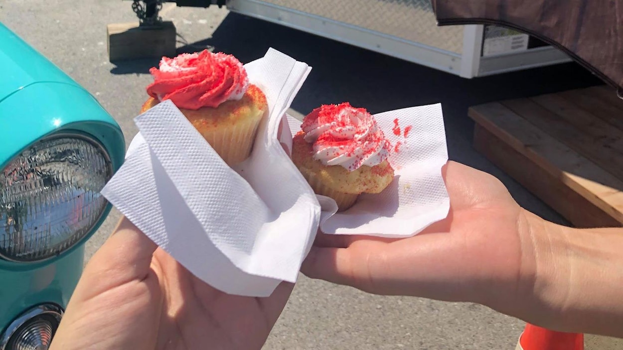 Deux cupcakes devant un comptoir mobile dans un stationnement.