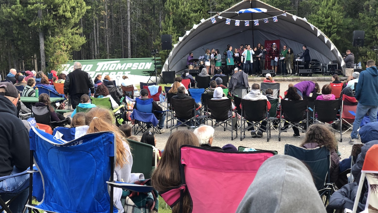 Des festivaliers sont assis sur des chaises de camping devant une scène aménagée à l'extérieur.