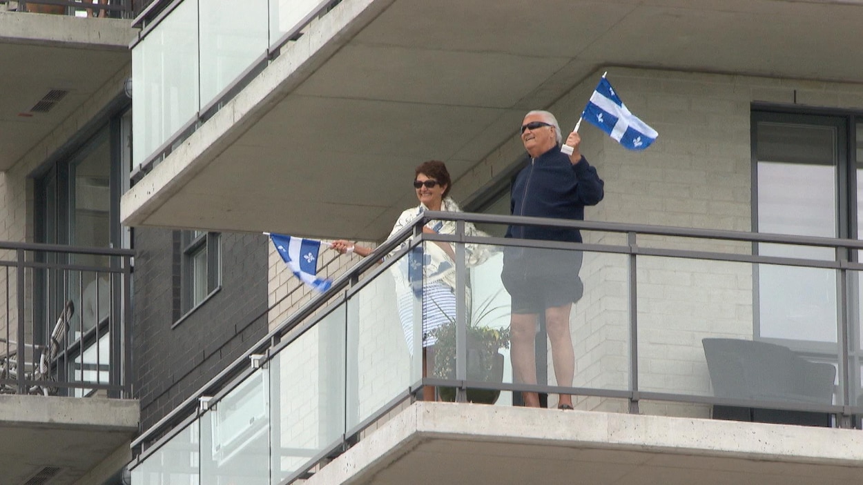 Un homme et une femme agitent chacun un drapeau du Québec sur leur balcon.