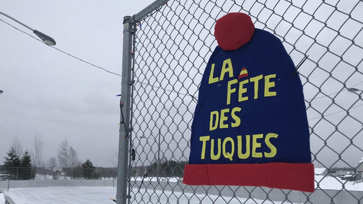 Une décoration représentant une grande tuque bleue portant l'inscription La fête des tuques est accrochée à une clôture
