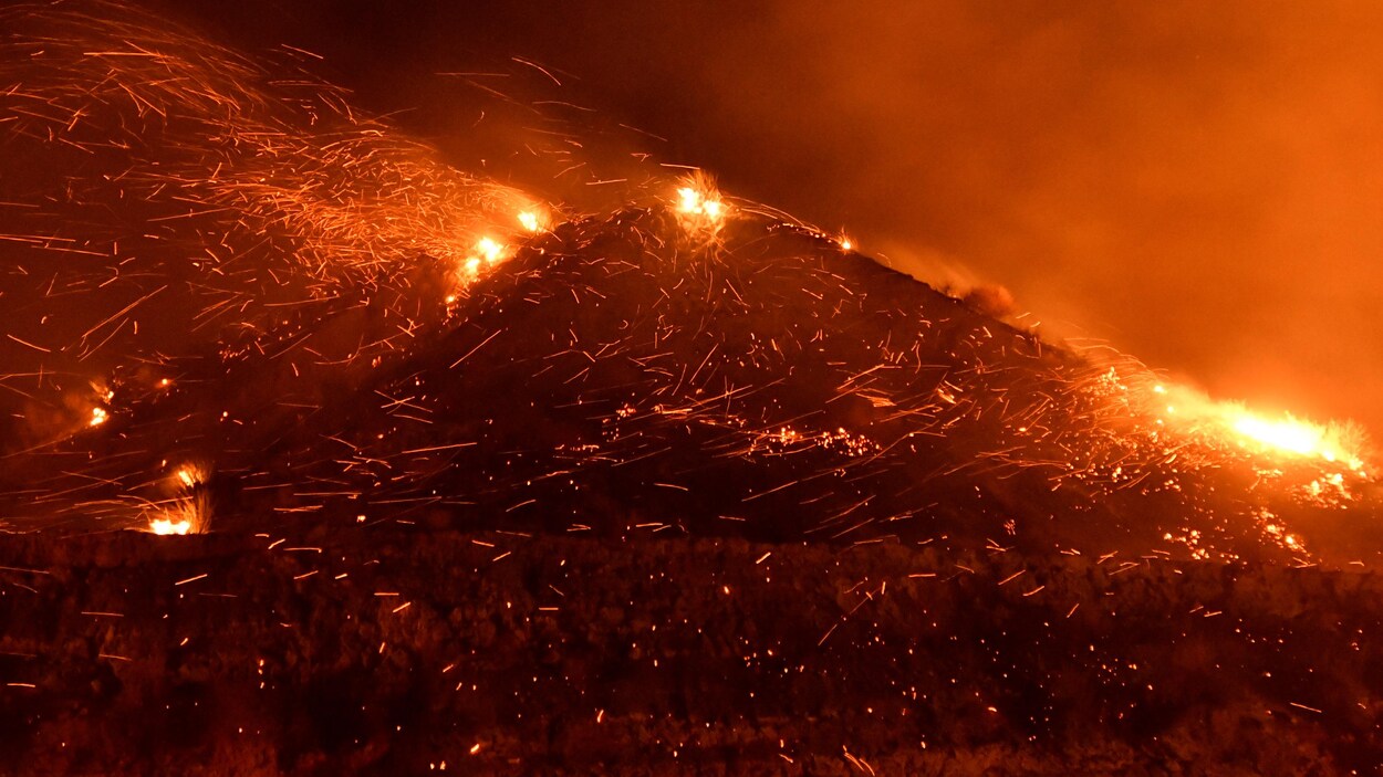 Dans la nuit, une montagne est ravagée par les flammes. Le vent souffle fort, faisant virevolter des tisons.