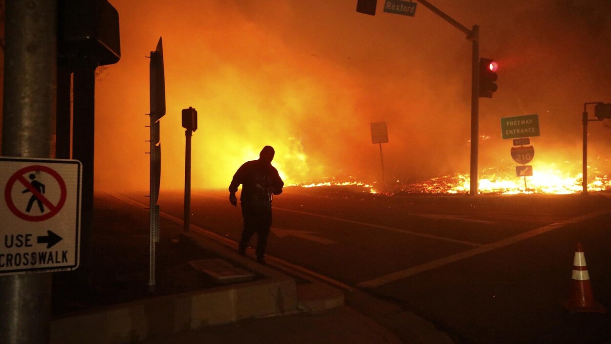 Un homme au coin d'une rue juste en face d'un feu immense.