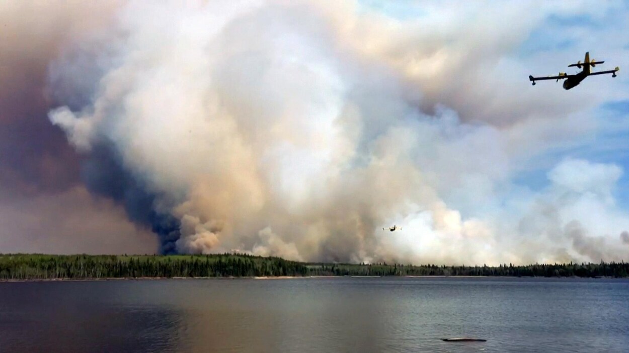 Deux avions-citernes se dirigent vers un immense panache de fumée issu d'un feu de forêt qui brûle près des terres de la Première Nation de Pauingassi