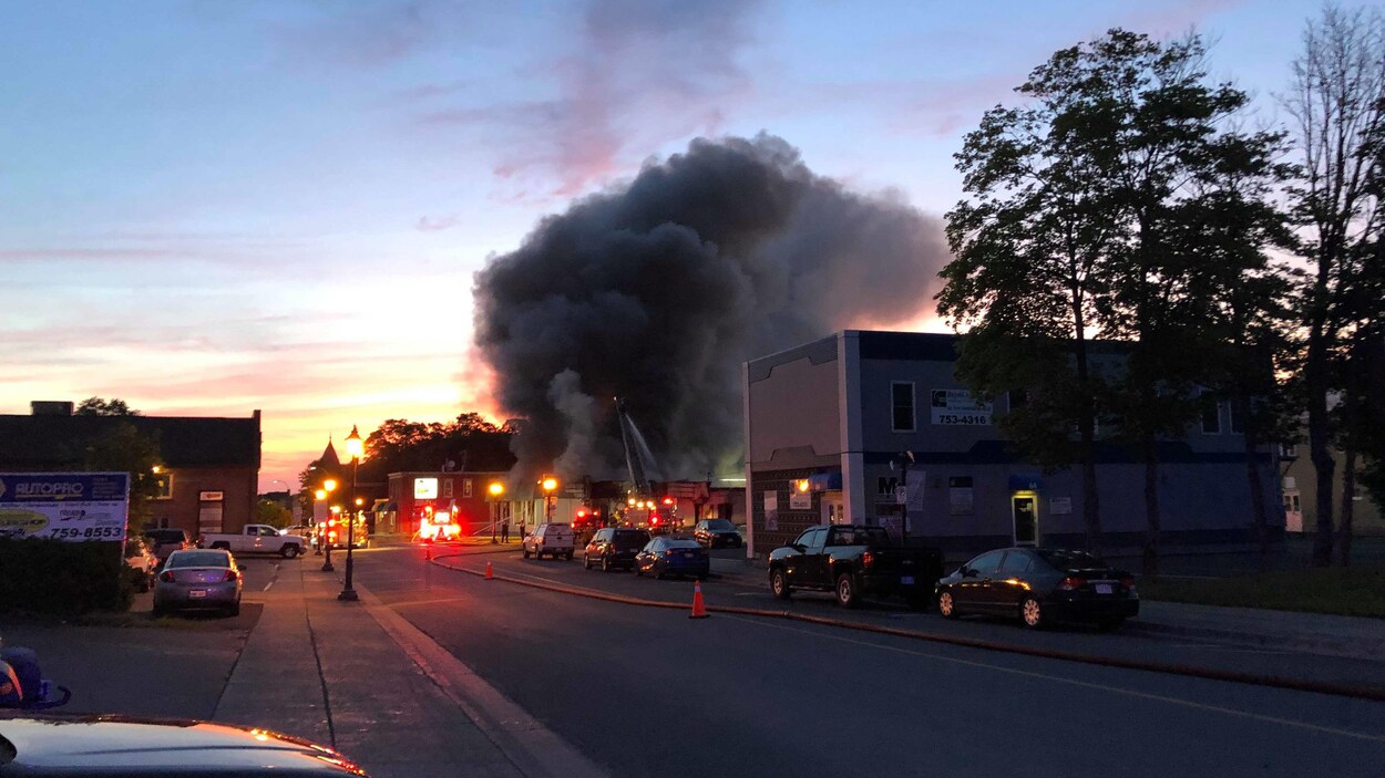 Une fumée dense s'échappe de l'édifice au loin, tandis que des pompiers tentent d'éteindre l'incendie.
