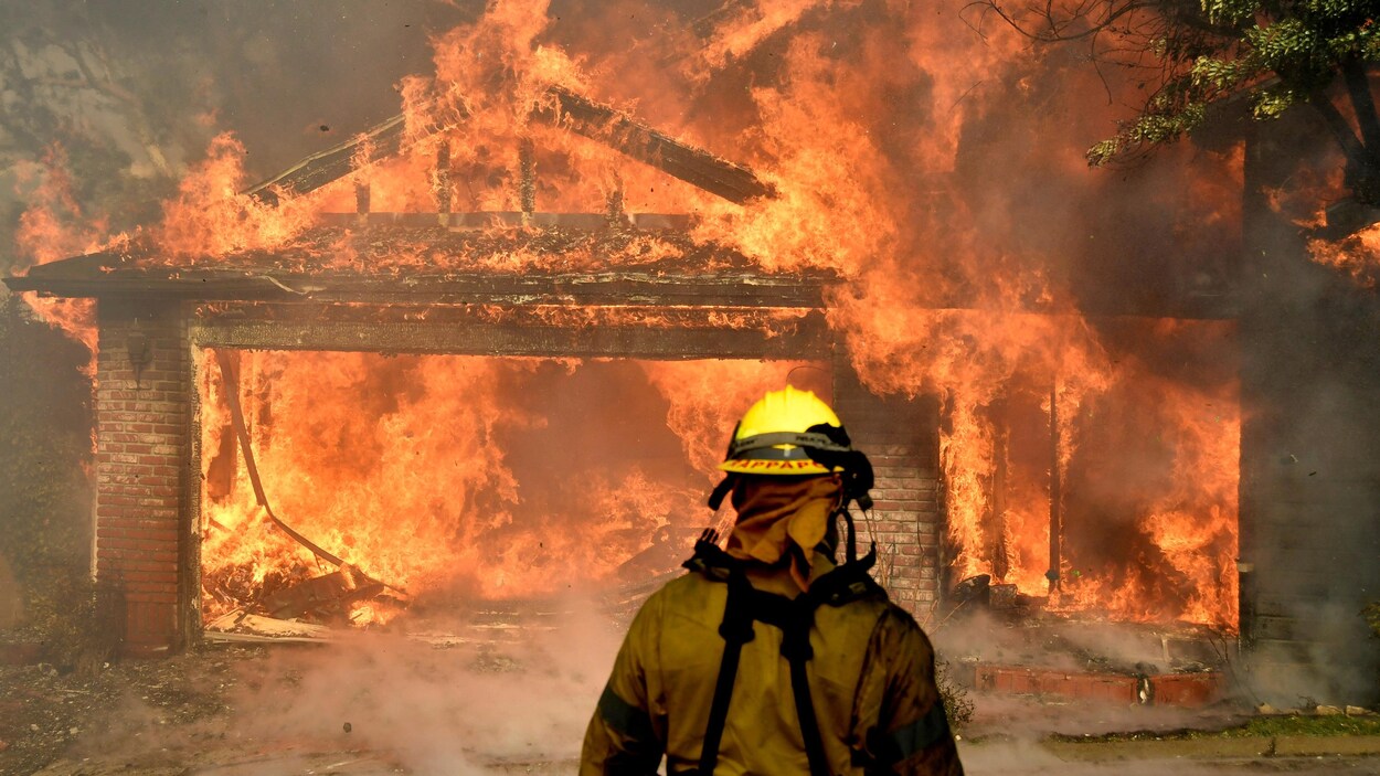 Un pompier devant une maison en flammes.