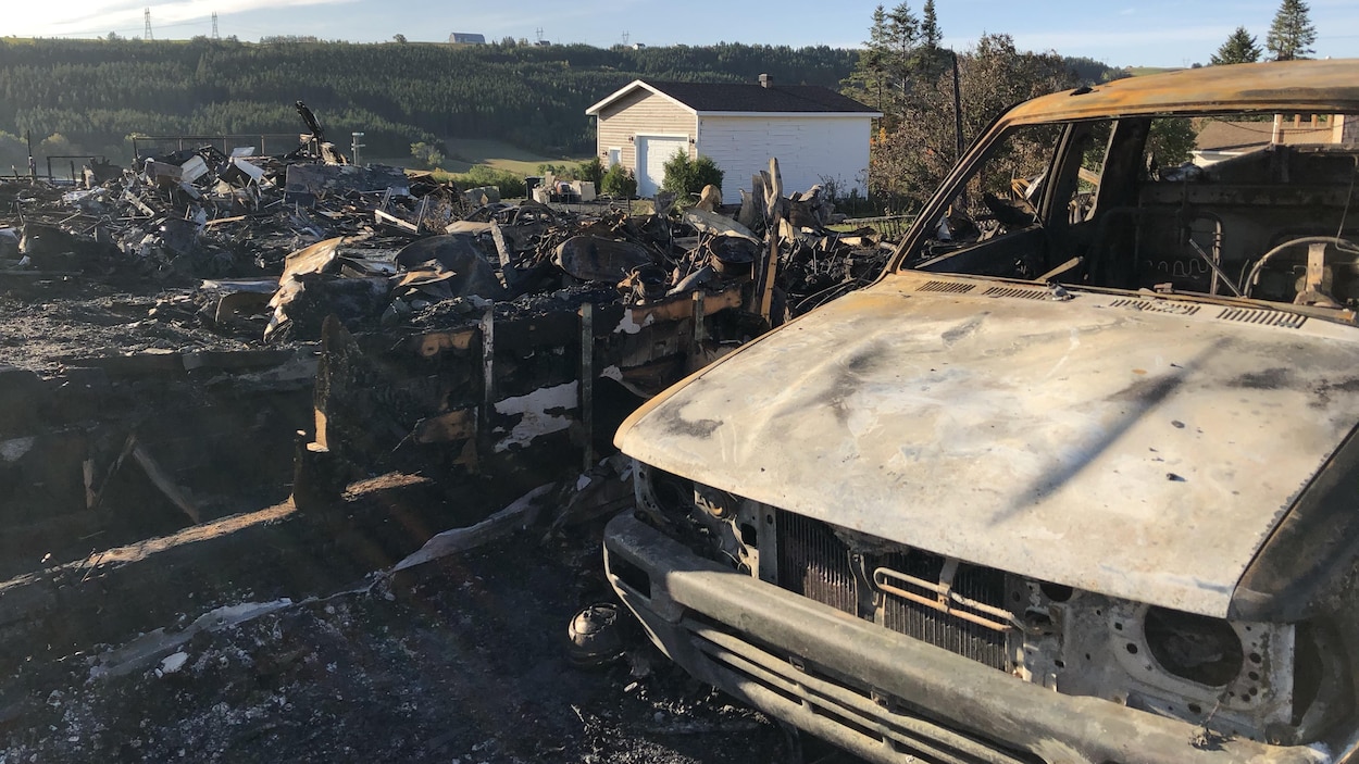 Une voiture calcinée devant une maison en cendres.