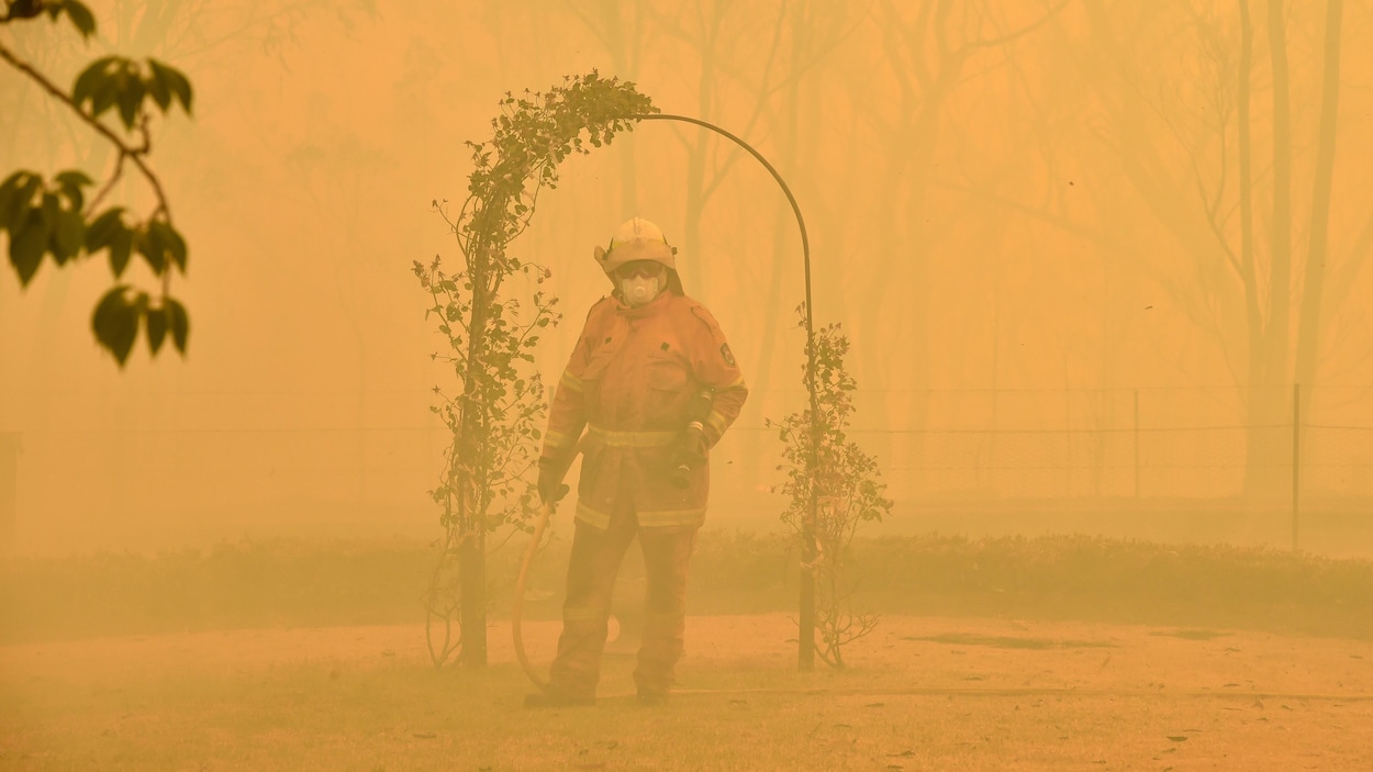 Un pompier combat un feu de forêt, encerclé par de la fumée. 