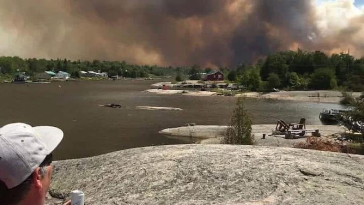 Une épaisse fumée derrière un lac et des arbres.