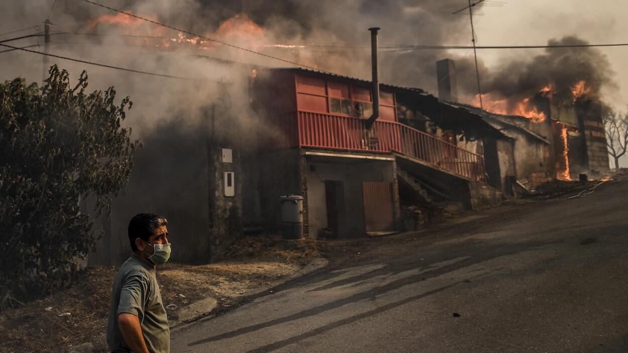 Un homme porte un masque pour se protéger de la fumée, alors que non loin de lui des édifices sont en flammes.