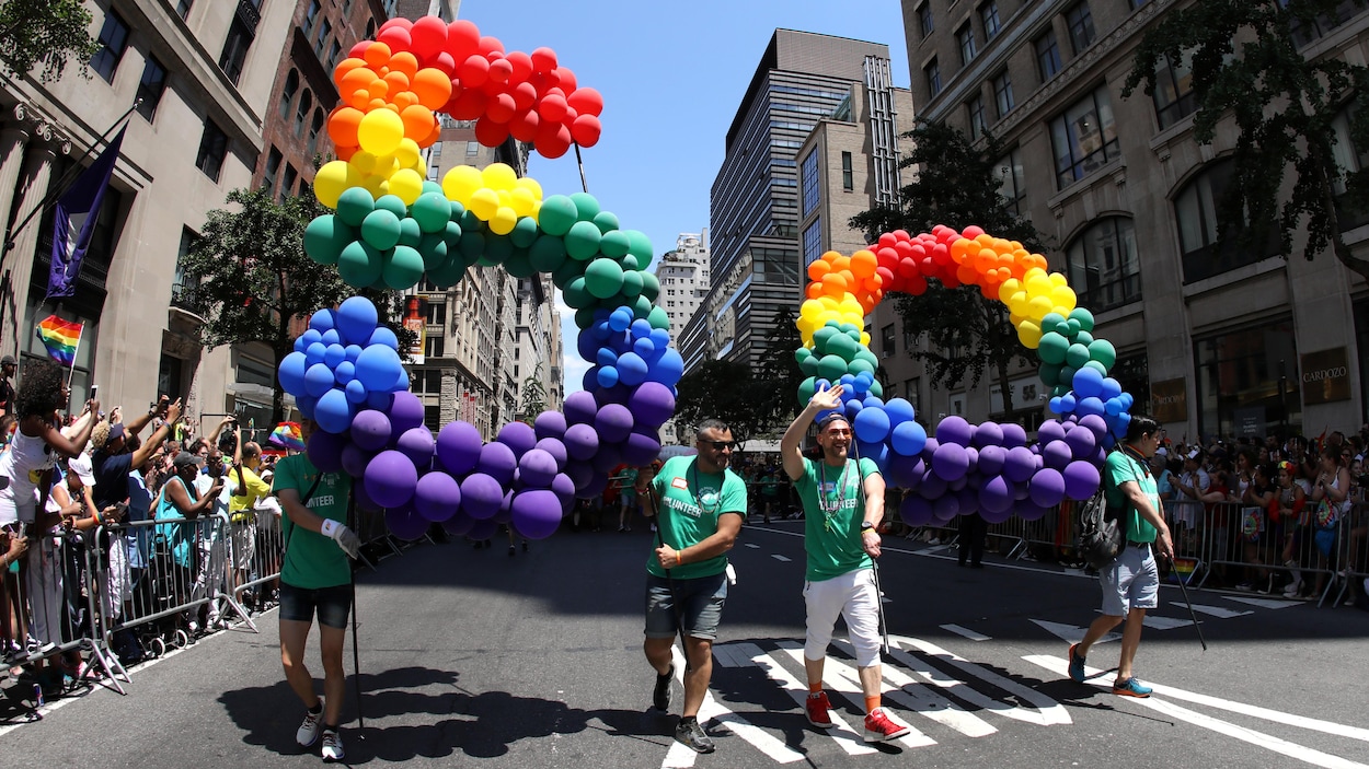 Quatre hommes participant au défilé tiennent un énorme 5 et un énorme 0 faits de ballons aux couleurs de l'arc-en-ciel.