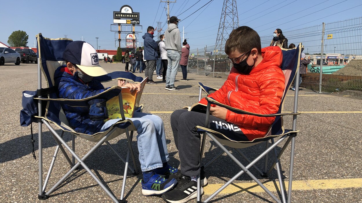 Deux enfants assis sur des chaises pliantes font la file pour un test de dépistage de la COVID-19.