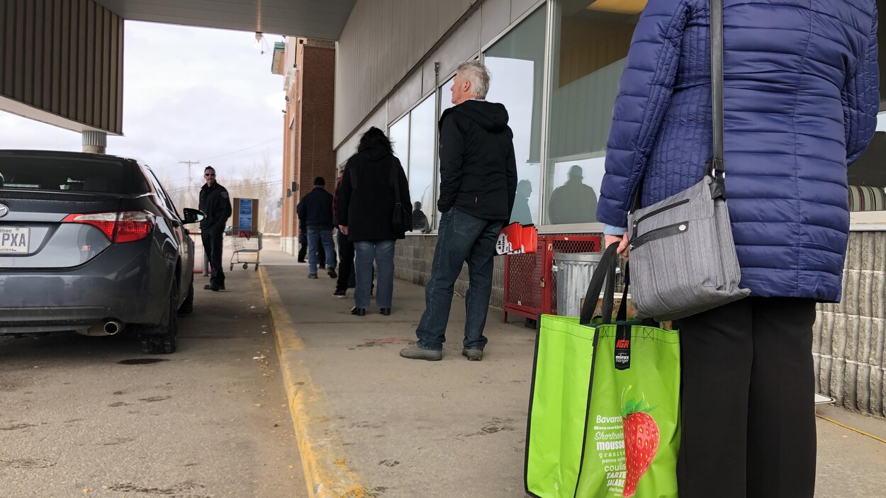 Une file d'attente de personne éloignées les unes des autres devant une épicerie.