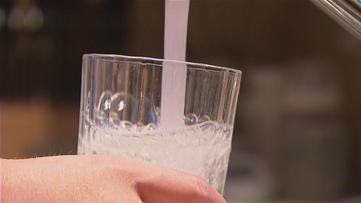 Plan serré d'eau provenant d'un robinet remplissant un verre tenu par une main.