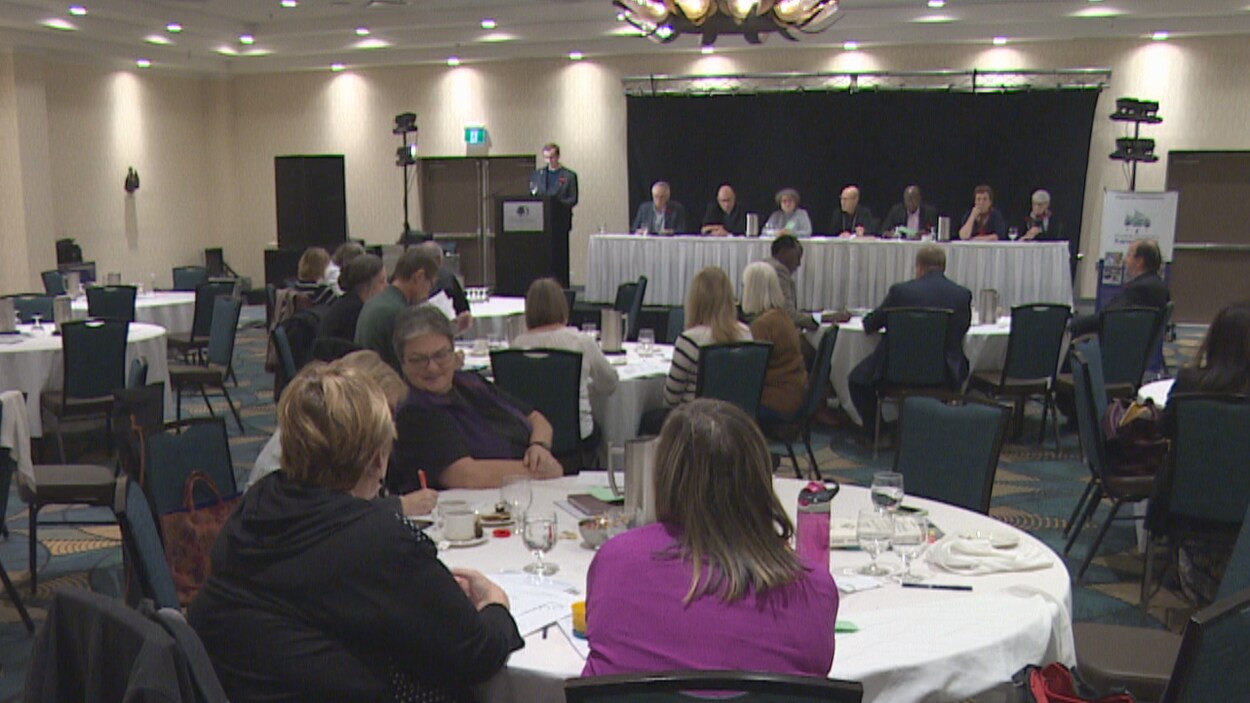 Des personnes attablées dans une salle de conférence.