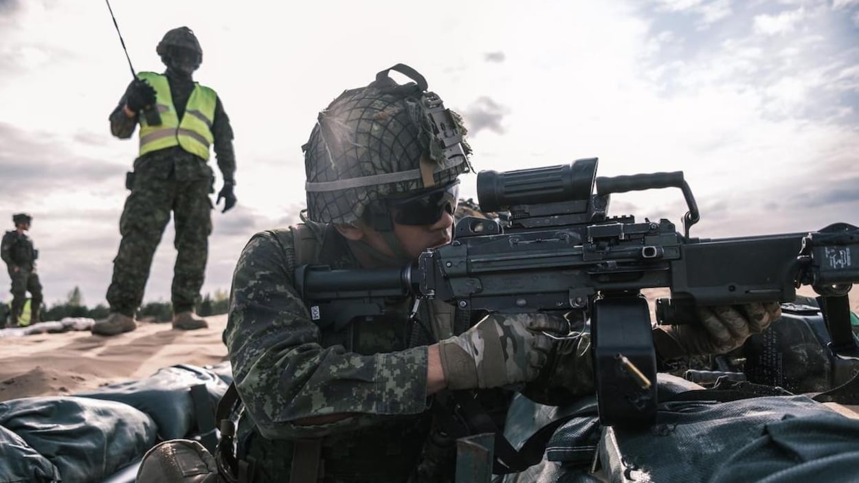 Un soldat équipé tire sous l'oeil d'un autre soldat qui supervise les opérations.