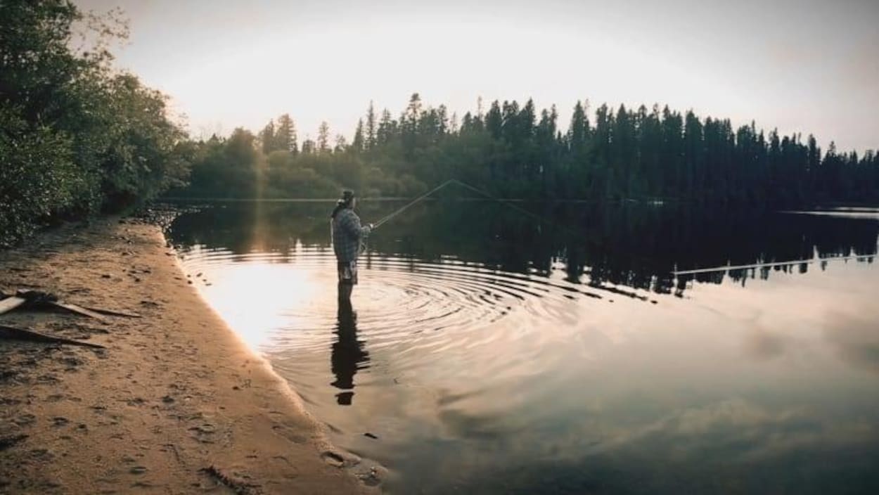 Vue sur un homme les pieds dans l'eau d'un lac et qui pêche Vue sur un homme les pieds dans l'eau d'un lac et qui pêche