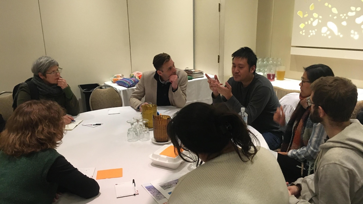 Sept personnes sont autour d'une table dans une salle de conférence et l'une d'entre elles parle de son idée pour créer un quartier innovant.