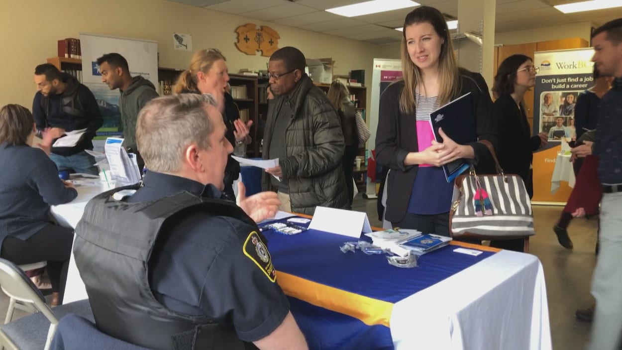 Un policier assis derrière une table sur laquelle se trouvent des prospectus de recrutement parle à une candidate potentielle.
