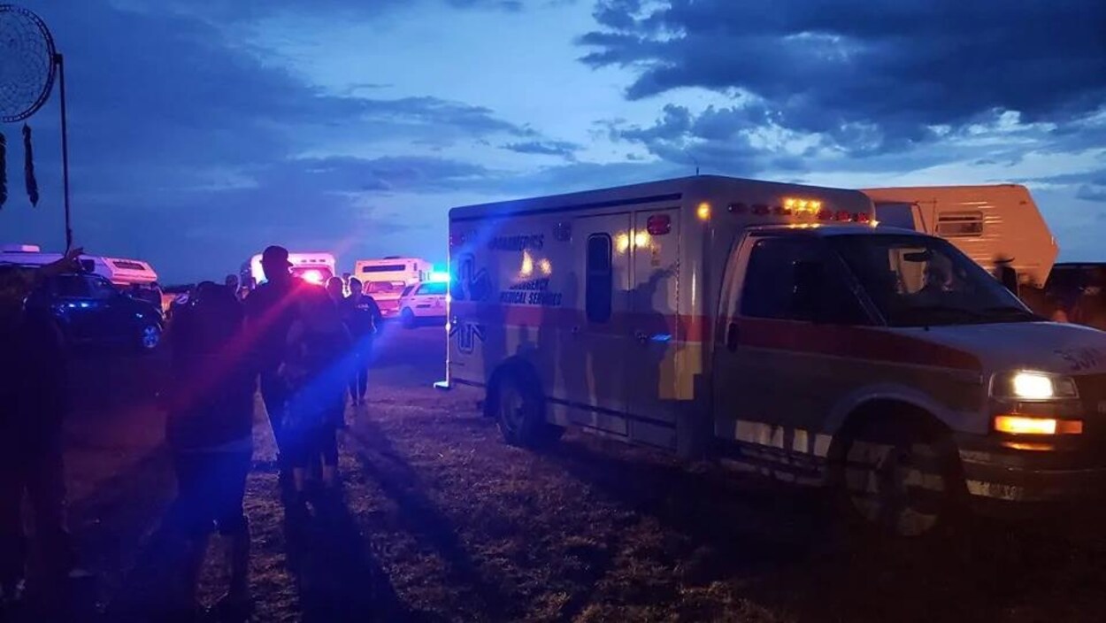 Une ambulance et des personnes sur un terrain sous un ciel nuageux.