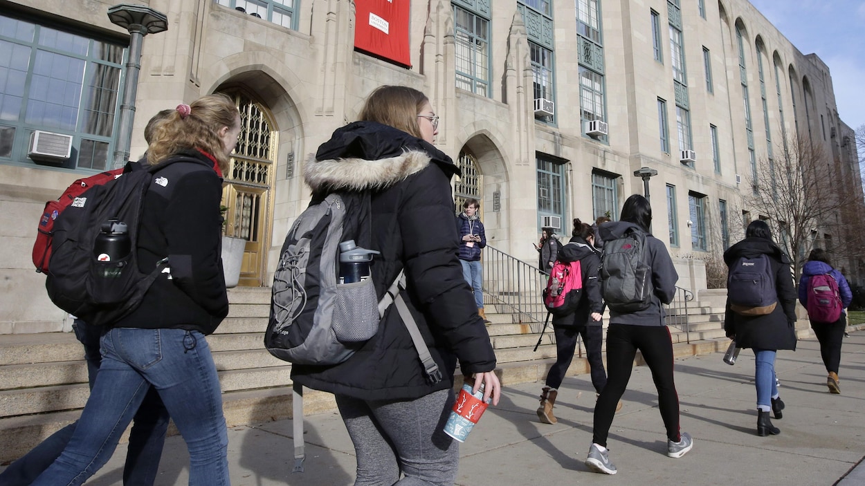 Des étudiants portant des sacs à dos marchent sur un campus universitaire.