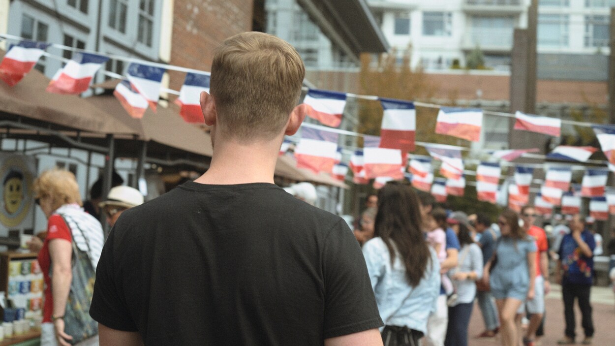 Un homme marche dans la foule. Des drapeaux français sont suspendus.