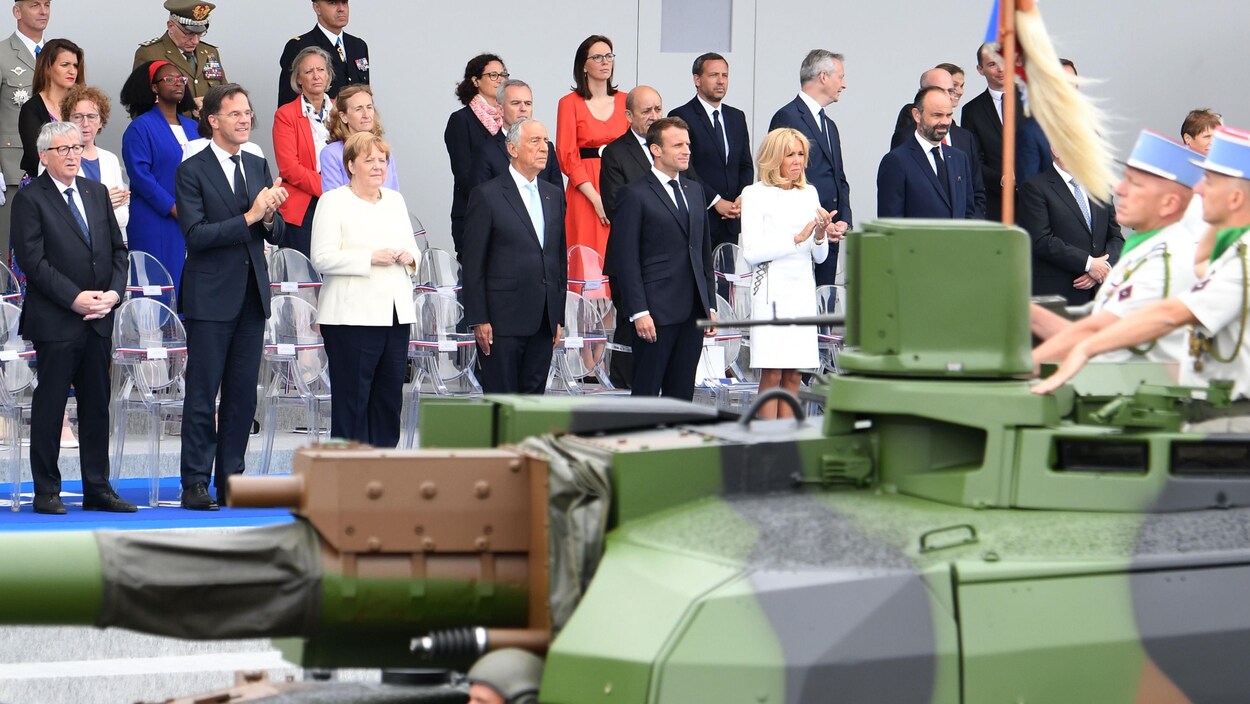 Une quinzaine de personnes dont Emmanuel Macron, Angela Merkel, Jean-Claude Juncker et Jens Stoltenberg regardent le défilé.