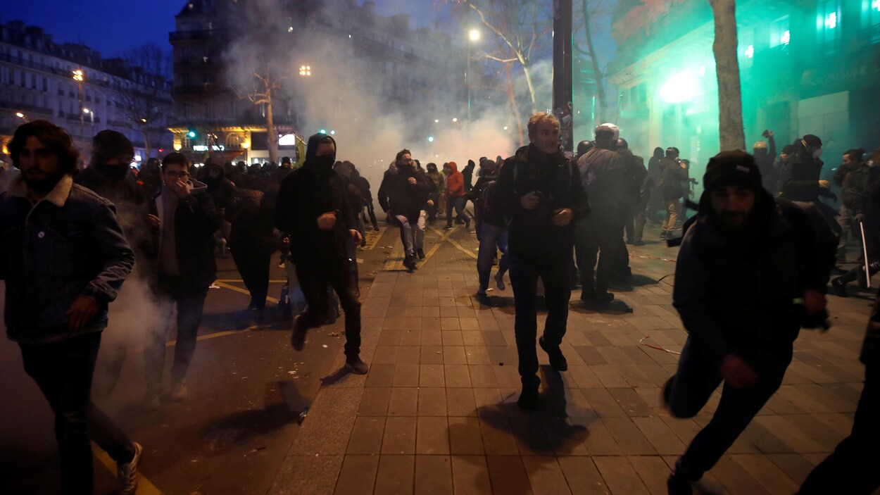 Plusieurs manifestants courent, entourés de gaz lacrymogènes.