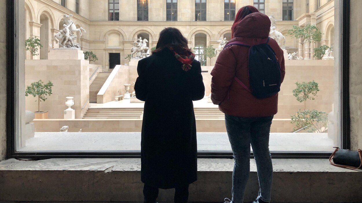 Deux femmes de dos regardent à travers une fenêtre.