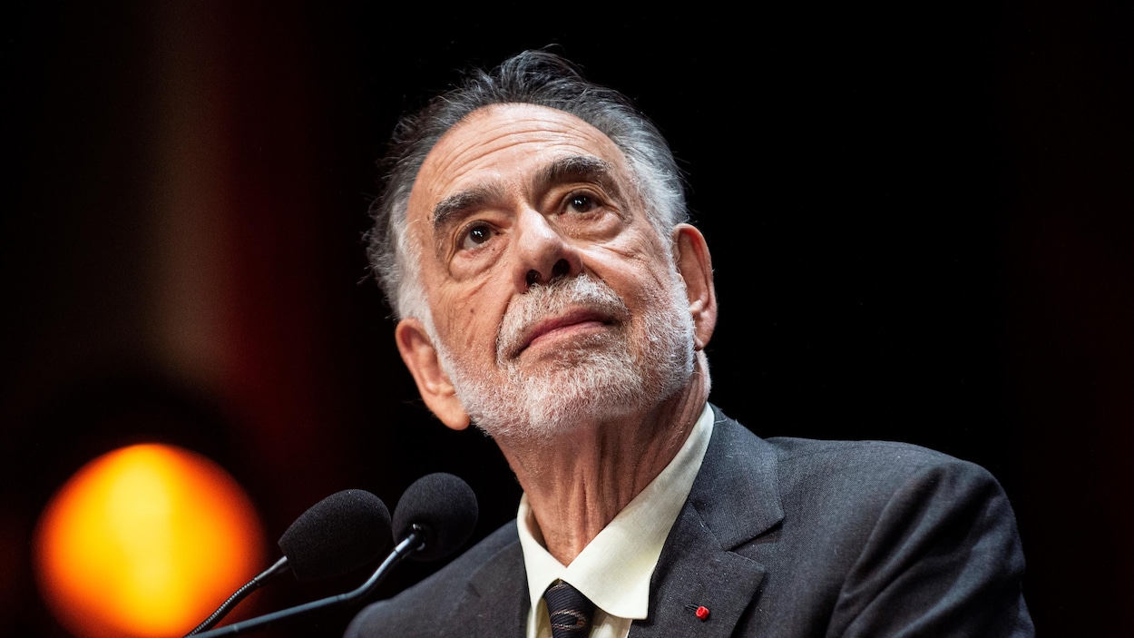Le cinéaste Francis Ford Coppola regarde de côté vers le haut devant deux microphones.