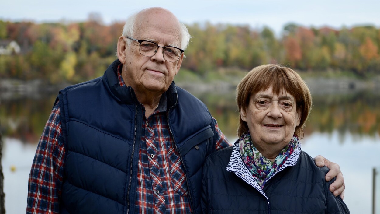 Les deux personnes qui posent dehors devant un lac et des arbres.