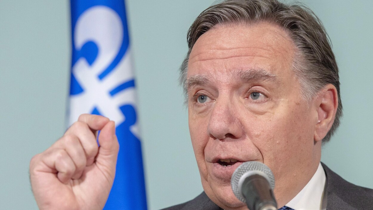 François Legault parle dans un micro, devant un drapeau du Québec.