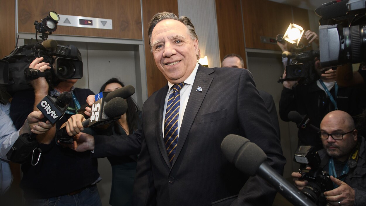 M. Legault est entouré de journalistes qui pointent vers lui caméras et micros.