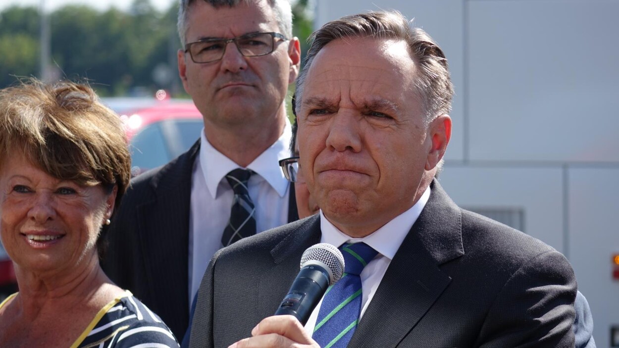 François Legault, les lèvres serrées, alors qu'on aperçoit notamment Éric Caire derrière lui.