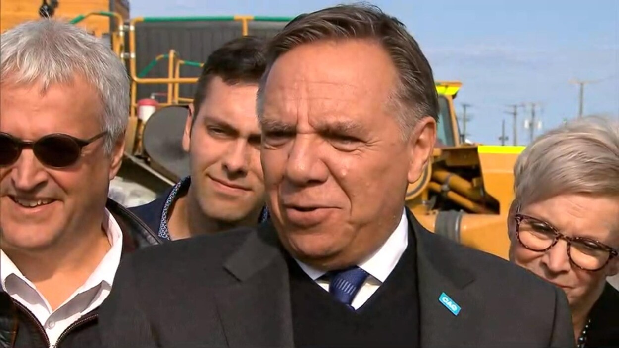 François Legault s'adresse aux médias devant un gros camion de couleur orange.