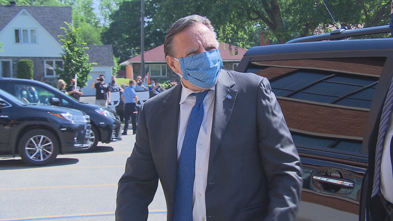 Le premier ministre François Legault sort d'une voiture dans un stationnement. Il porte un couvre-visage.