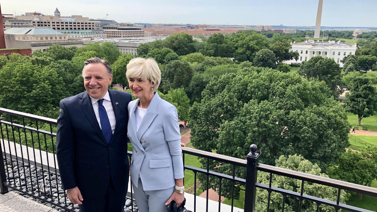 François Legault et Isabelle Brais posent sur un balcon, la Maison-Blanche apparaît en arrière-plan.