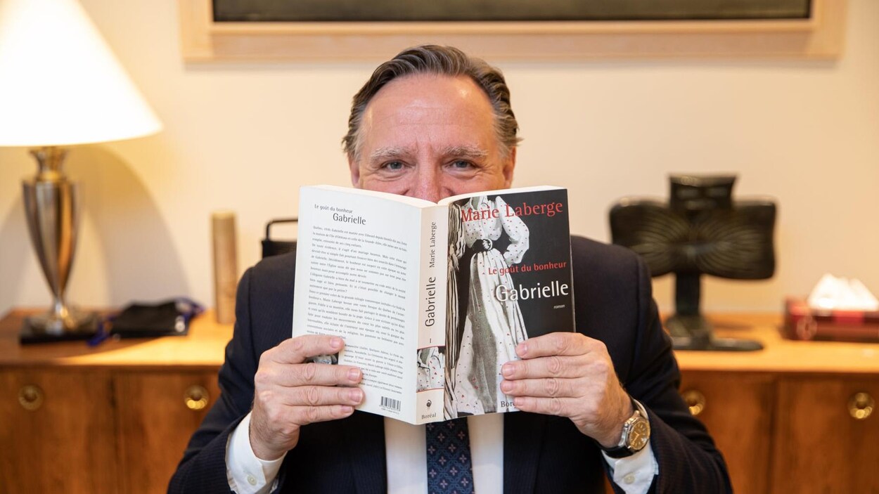L'homme tient le premier tome de la trilogie, « Gabrielle », dans ses mains, devant son visage.